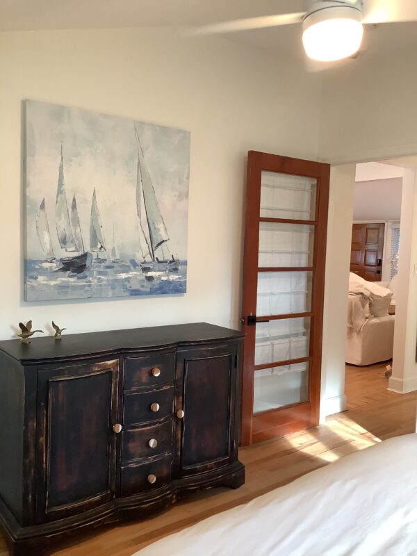 A painting of boats on the water is hanging in a bedroom.